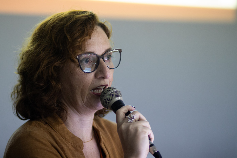 Mulher ruiva usando óculos fala ao microfone